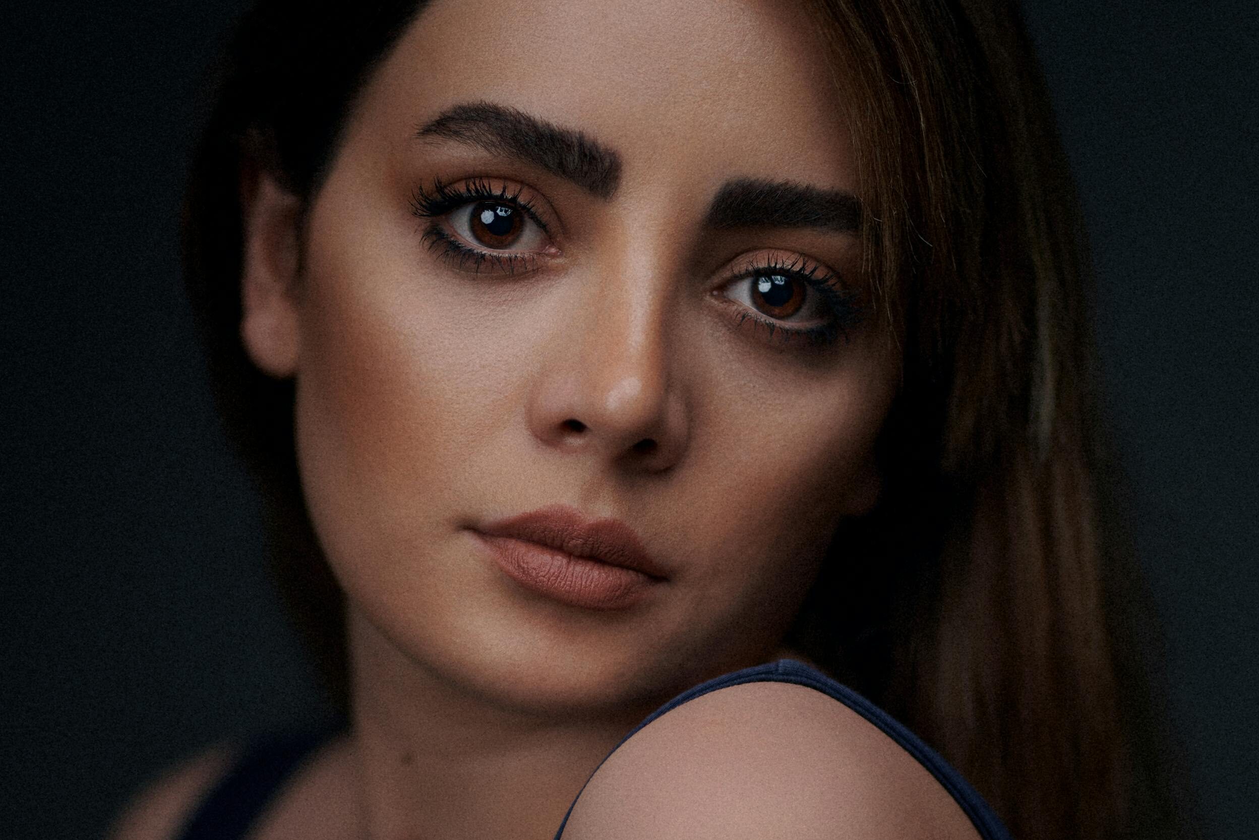 Close-up portrait of a woman with long hair and natural makeup against a dark background.